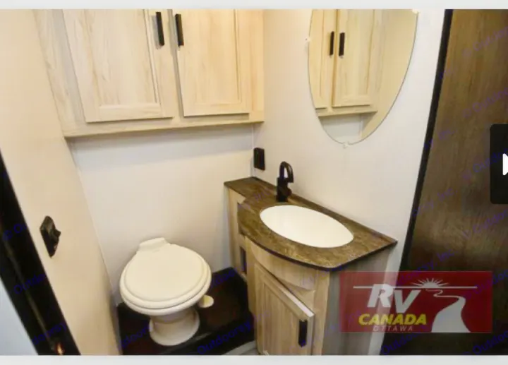 Compact RV rental bathroom with a toilet, vanity sink, mirror, and overhead wood-look cabinets. Efficient design for travel.. Forest River Sunseeker LE 2023