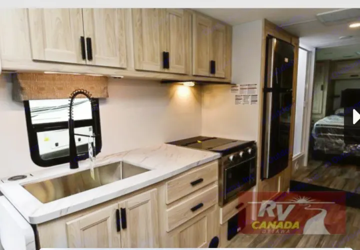 Spacious RV rental interior: a modern kitchen with light wood cabinets, stone counters, stove, fridge, and glimpse of the bedroom.. Forest River Sunseeker LE 2023
