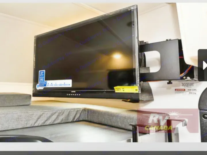 Flat-screen TV on articulating mount extends over gray upholstered seating in an RV rental interior, perfect for leisure.. Forest River Sunseeker LE 2023