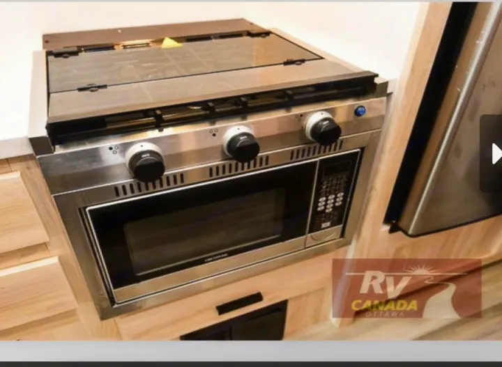 Inside an RV rental: a compact kitchen unit with a stainless steel gas stovetop, glass cover, and built-in microwave.. Forest River Sunseeker LE 2023