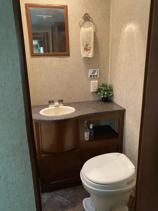 Compact RV rental bathroom with a sink, mirror, and toilet, offering essential amenities in a small, functional space.. Heartland RVs 30LX 2014