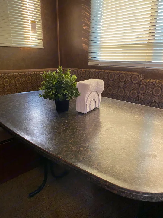 RV rental dinette: a table with a faux plant & napkins, patterned bench seating. Sunlight shines through window blinds.. Heartland RVs 30LX 2014