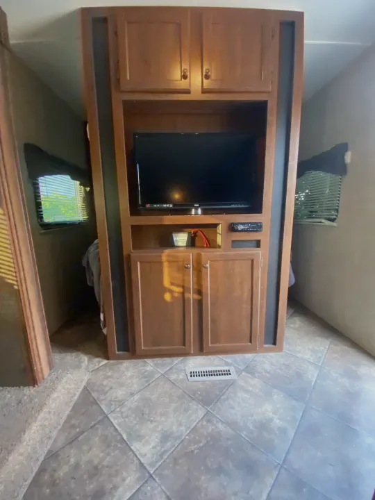 This RV rental interior features a sturdy wooden entertainment center with a TV, ample storage, and practical tile flooring.. Heartland RVs 30LX 2014