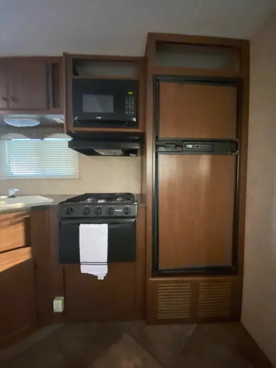 RV rental interior: cozy kitchen with wood cabinets, microwave, 4-burner stove, refrigerator, and sink setup.. Heartland RVs 30LX 2014