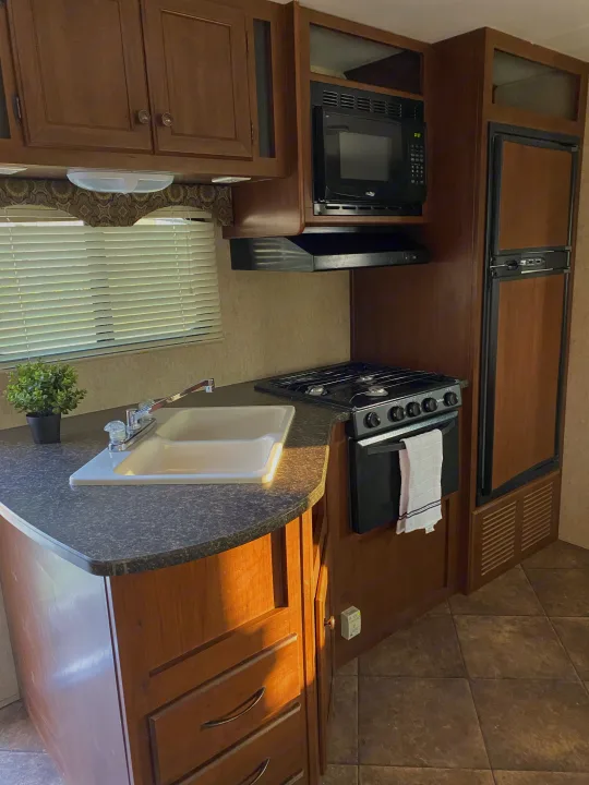 RV rental: well-appointed compact kitchen featuring wood cabinets, sink, stove, microwave, and fridge.. Heartland RVs 30LX 2014