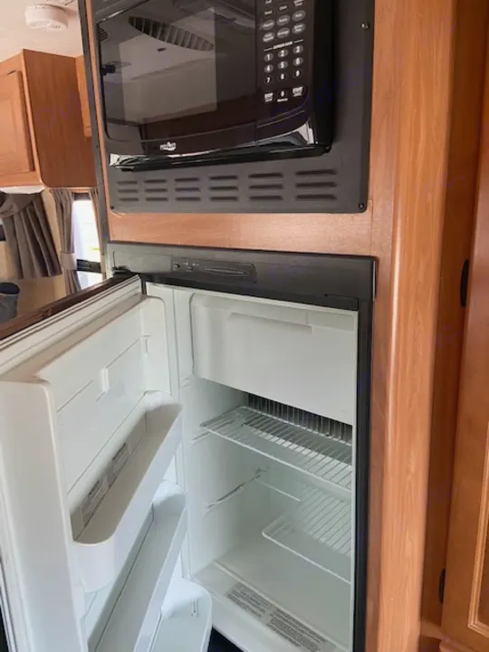 Inside an rv rental: a compact kitchen space featuring a black microwave and an open, empty refrigerator.. Thor Majestic 2016