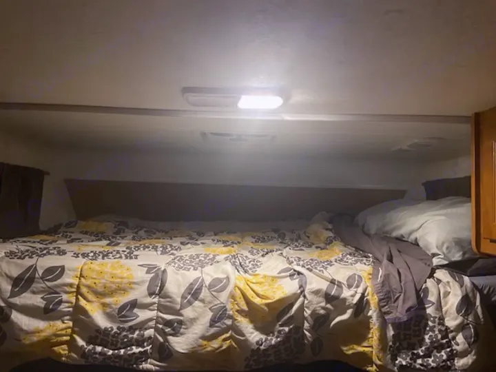 Cozy RV rental bed with a floral comforter and pillows under bright ceiling lights. Perfect for a comfortable night in your camper.. Thor Majestic 2016