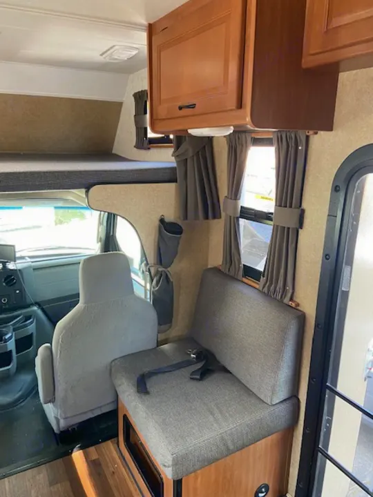RV rental interior: light wood cabinets, cozy grey seating, windows with curtains, and sturdy wood-look flooring.. Thor Majestic 2016