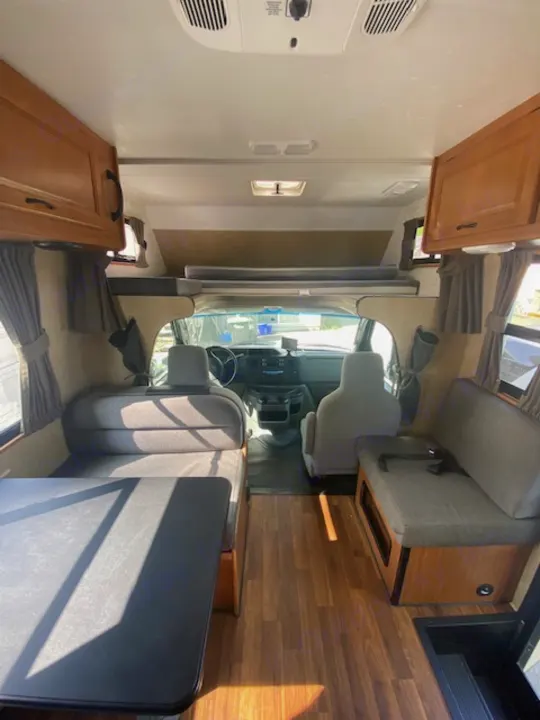 RV rental interior featuring the driver's cockpit, a comfortable dinette, wood-look flooring, and overhead cabinets.. Thor Majestic 2016