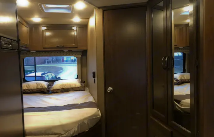 RV rental's inviting bedroom: a comfortable bed with pillows, overhead cabinets, window, and mirrored wardrobe.. Thor Four Winds 2018