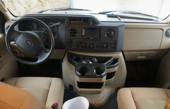 RV rental's Ford E-Series cockpit: driver's perspective of dashboard, steering wheel, and beige front seats.. Thor Four Winds 2018