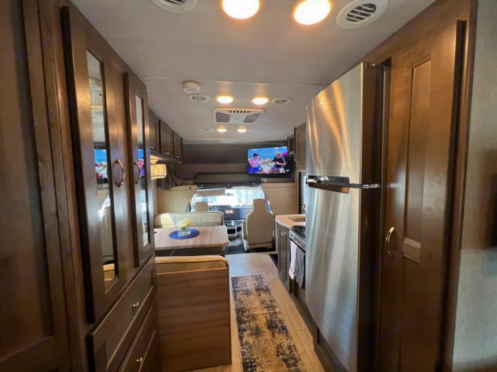 Experience comfort in this RV rental! View of kitchen, dining nook, and front cabin with TV, featuring wood cabinetry & stainless fridge.. Nexus Triumph 23T 2020