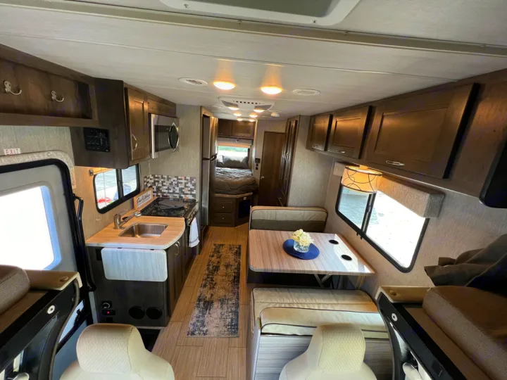 Spacious RV rental interior with a fully equipped kitchen, dining area, and a cozy bedroom at the back.. Nexus Triumph 23T 2020