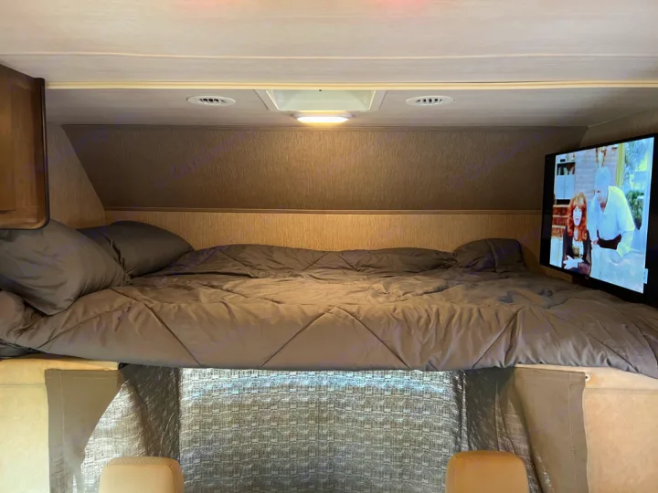 Inviting gray bed and pillows in an RV rental, complete with a wall-mounted TV for entertainment.. Nexus Triumph 23T 2020