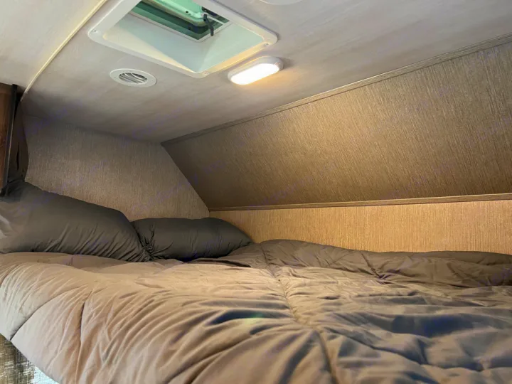 Cozy rv rental sleeping area with gray bedding, overhead vent, and light fixture, ready for a restful night.. Nexus Triumph 23T 2020