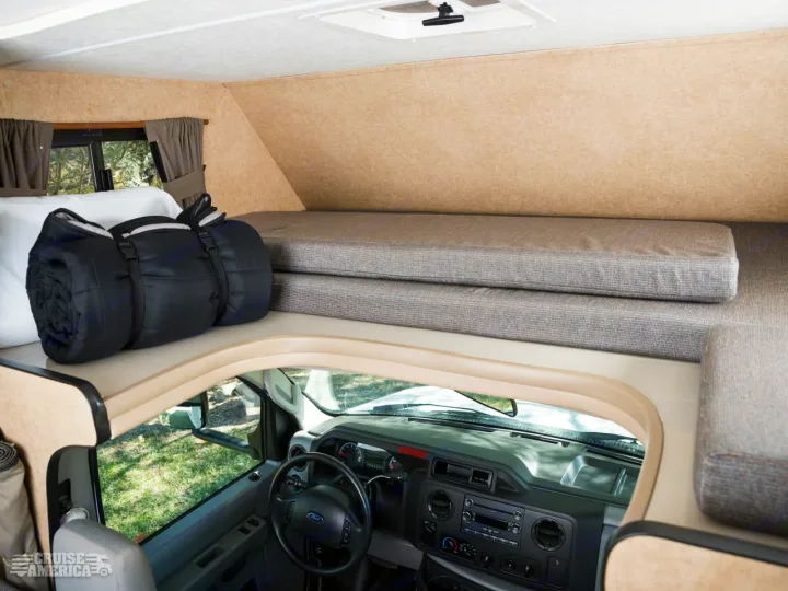 Spacious rv rental interior, featuring an overhead sleeping bunk with a rolled sleeping bag & mattresses, above the driver's cab.. Thor Majestic 2016