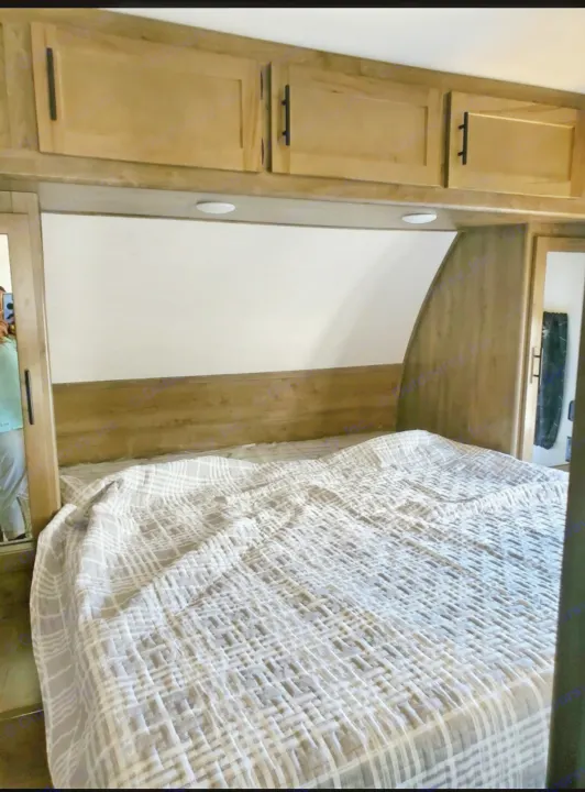 Inside a comfortable RV rental bedroom featuring a plaid-patterned bed, wood cabinets, and task lighting.. Forest River Cherokee Wolf Pack Toy Hauler 2022