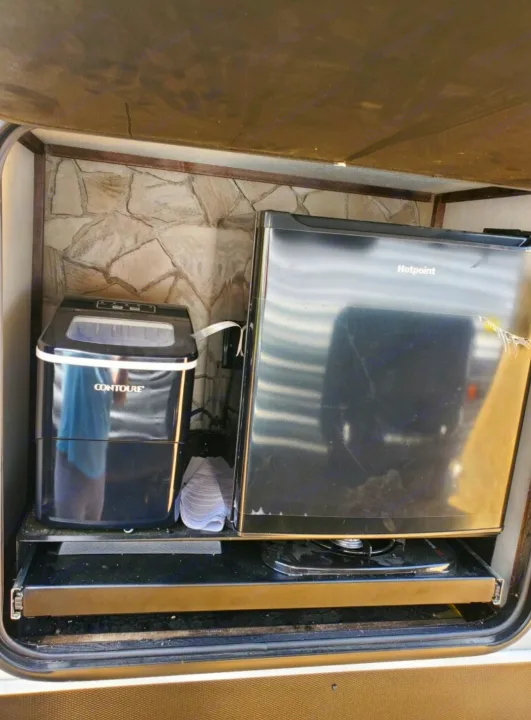 Inside an RV rental's outdoor kitchen: a Hotpoint mini-fridge, Contoure ice maker, and pull-out cooking burner.. Forest River Cherokee Wolf Pack Toy Hauler 2022
