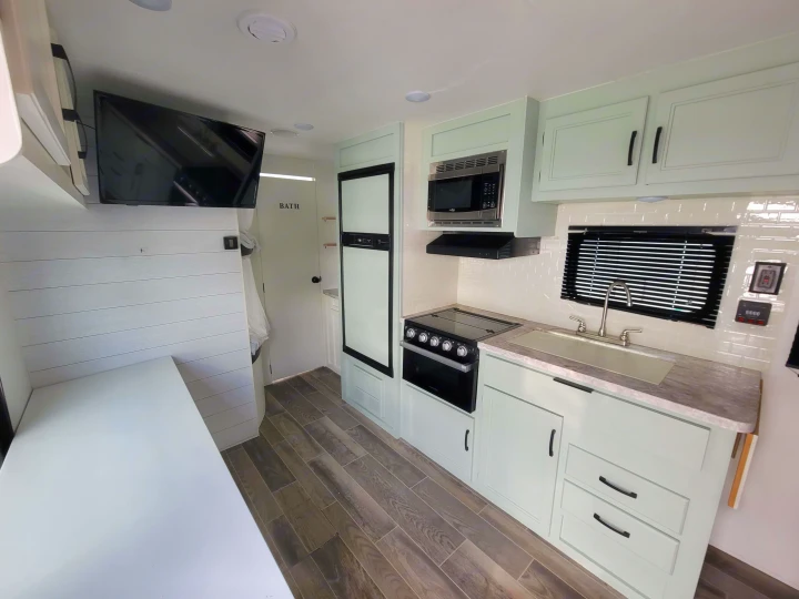 RV rental interior features a bright kitchen with light green cabinets, modern appliances, sink, and dining/living area with TV and shiplap.. Jayco Jay Flight SLX 2021