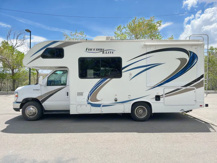 White Freedom Elite Class C RV rental parked on asphalt, featuring blue and tan graphics on a sunny day.. Thor Motor Coach Freedom Elite 2018