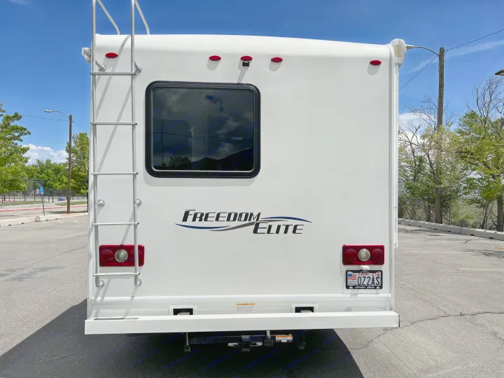 Rear view of a white Freedom Elite RV rental, showing its ladder, rear window, taillights, and Utah license plate in a parking lot.. Thor Motor Coach Freedom Elite 2018