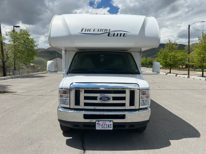 Front view of white Class C rv rental with 'Freedom Elite' branding, parked in lot. Utah plate visible.. Thor Motor Coach Freedom Elite 2018