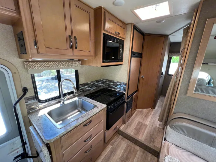 Step inside this modern rv rental kitchen, featuring light wood cabinets, a stainless sink, stove, microwave, and fridge.. Thor Motor Coach Freedom Elite 2018