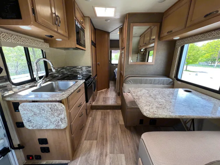 Spacious RV rental interior featuring a full kitchen with sink, stove, microwave, and a cozy dinette area.. Thor Motor Coach Freedom Elite 2018
