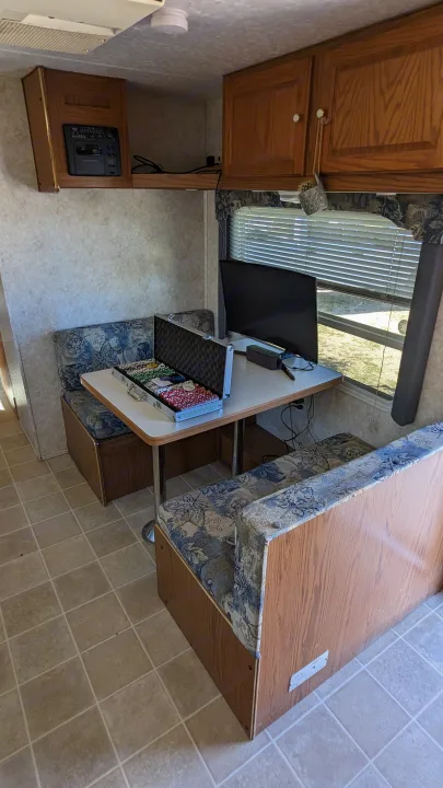 Inside an RV rental: a cozy dinette setup with a poker chip set, monitor, and floral-patterned booth seating.. Forest River Wildwood 2005