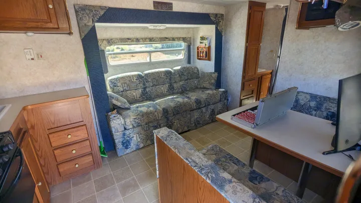Explore this RV rental's inviting living area with a floral couch, dinette, and kitchen. Ideal for road trip adventures.. Forest River Wildwood 2005