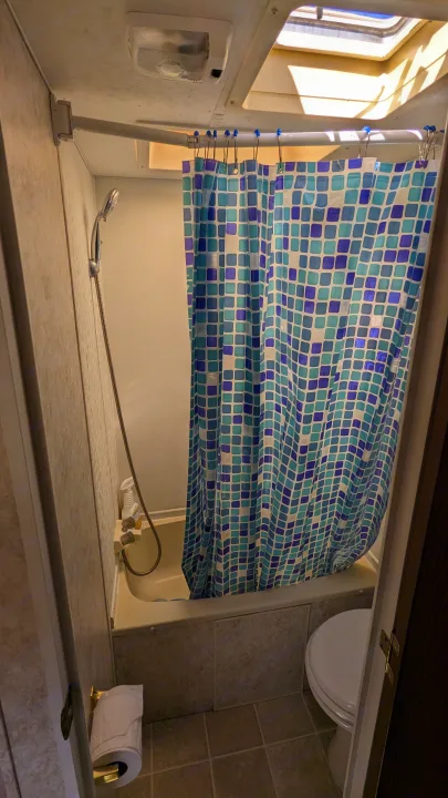 This rv rental features a compact bathroom with a shower (blue patterned curtain), toilet, and overhead skylight.. Forest River Wildwood 2005