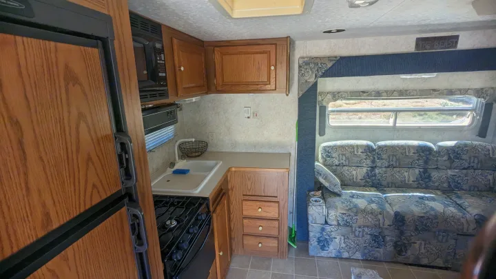 RV rental interior: Kitchen features fridge, microwave, stove; living area boasts a floral sofa and window views.. Forest River Wildwood 2005