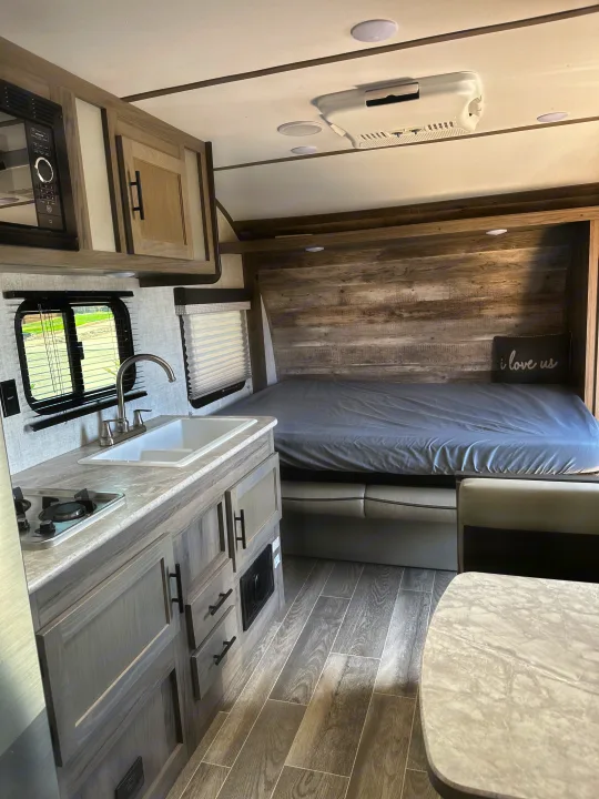 RV rental interior: A compact kitchen with microwave, sink & stove, alongside a bed & dining area in a modern travel trailer.. Gulf Stream Ameri-Lite Super Lite 2022