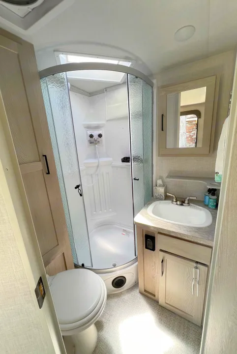 This RV rental features a bright, compact bathroom with a glass corner shower, toilet, and a vanity with sink.. Forest River Rockwood Roo 235S