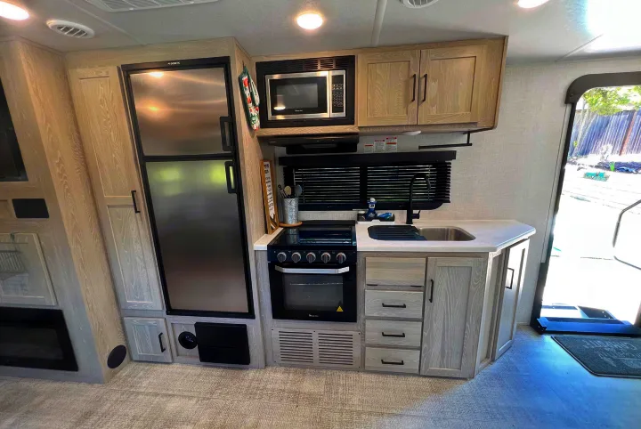 Modern RV rental kitchen. Features include stainless steel fridge, microwave, stove/oven, sink, and ample light-toned cabinetry.. Forest River Rockwood Roo 235S