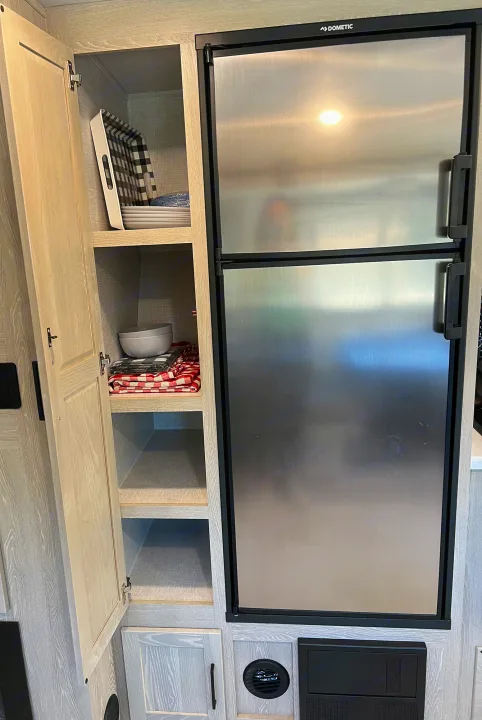 RV rental kitchen featuring a Dometic refrigerator and open pantry cabinet with dishes and towels.. Forest River Rockwood Roo 235S