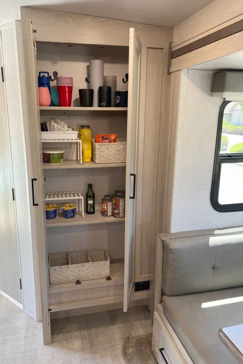 Organized RV rental kitchen pantry filled with cups, canned goods, and food, featuring clever storage racks and baskets.. Forest River Rockwood Roo 235S