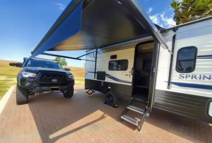 Discover freedom with this RV rental: A modern travel trailer with awning and a black Toyota Tacoma, ideal for camping adventures.. Keystone RV Springdale 2022