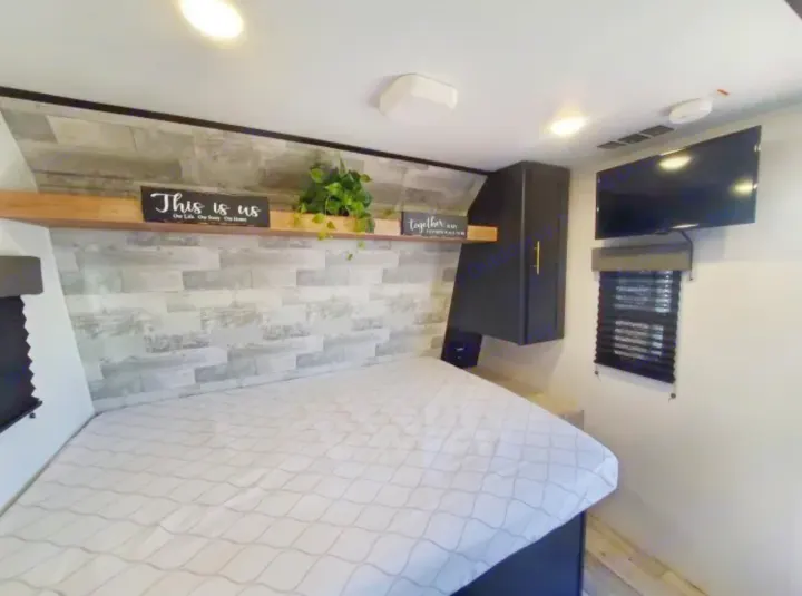 Cozy RV rental bedroom, featuring a patterned bed, decorative wood-paneled wall, storage, TV, and window for comfortable travel.. Keystone RV Springdale 2022