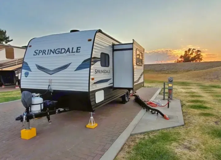 Springdale RV rental parked at a paved campsite with hookups, slide-out extended, under a beautiful sunset sky.. Keystone RV Springdale 2022