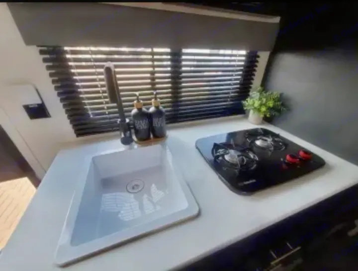 Compact RV rental kitchen with a sleek white countertop, sink, black faucet, and two-burner stove beside a window.. Keystone RV Springdale 2022