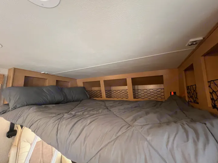 RV rental: Comfy bed with gray bedding, featuring wooden overhead storage cubbies & nets, ideal for travel.. Thor Motor Coach A.C.E 2017