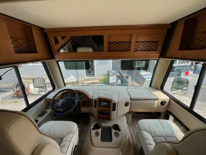 Spacious RV rental cockpit featuring light-colored seats, steering wheel, dashboard, and overhead storage.. Thor Motor Coach A.C.E 2017