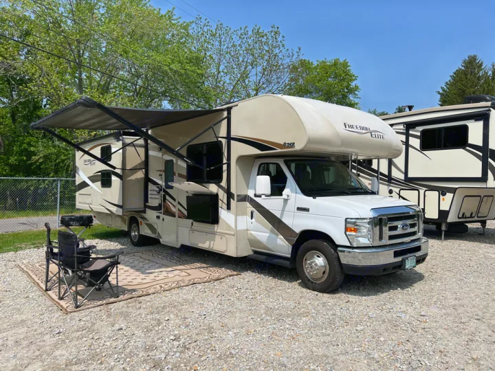 Enjoy a comfortable outdoor setup with this Class C RV rental, featuring an extended awning, chairs, rug, and grill for camping.. Thor Motor Coach Freedom Elite 2017