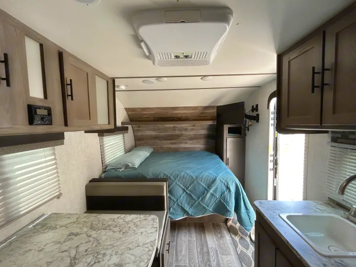 RV rental interior with a cozy bed, dinette, modern cabinetry, and compact kitchen sink area, ready for travel.. Gulf Stream Ameri-Lite Super Lite 2021