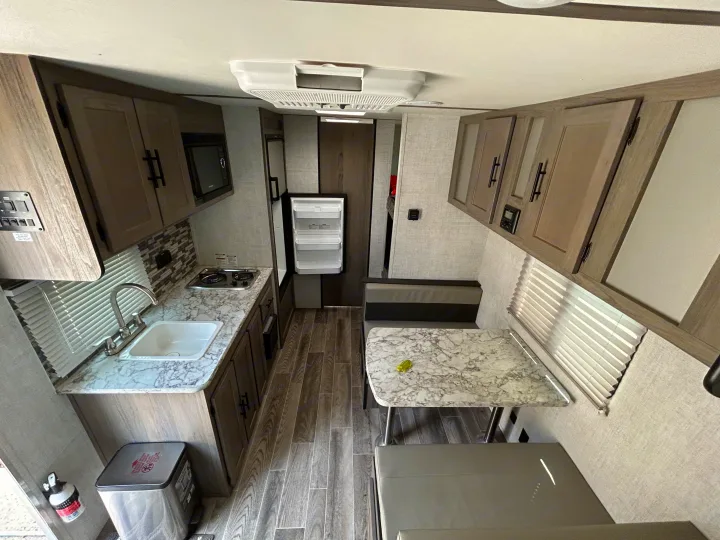 Inside an RV rental: a modern kitchen with sink and stove, dining booth, fridge, and stylish wood-look floor.. Gulf Stream Ameri-Lite Super Lite 2021