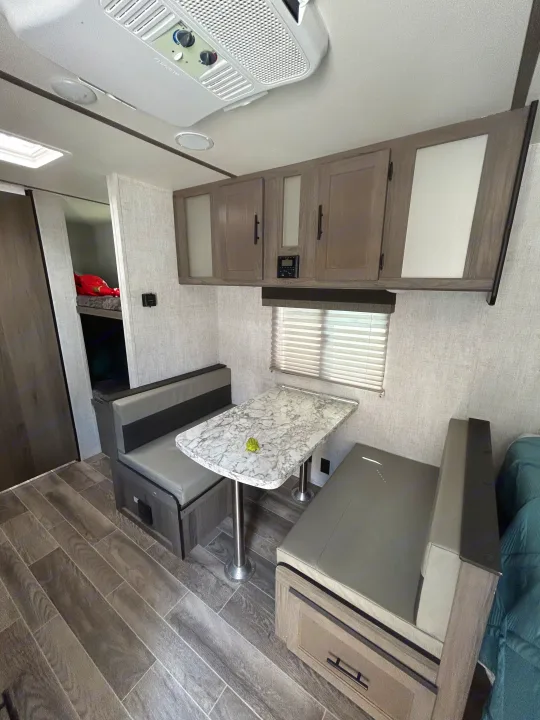 RV rental interior: Dinette with grey benches, marble-top table, overhead cabinets, and bunk beds.. Gulf Stream Ameri-Lite Super Lite 2021