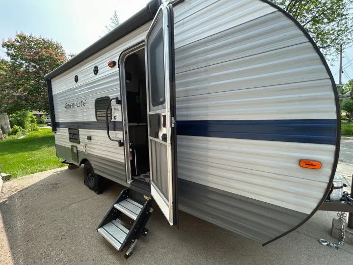 Ameri-Lite RV rental, a light-colored travel trailer with a dark blue stripe, features an open door and extended steps.. Gulf Stream Ameri-Lite Super Lite 2021