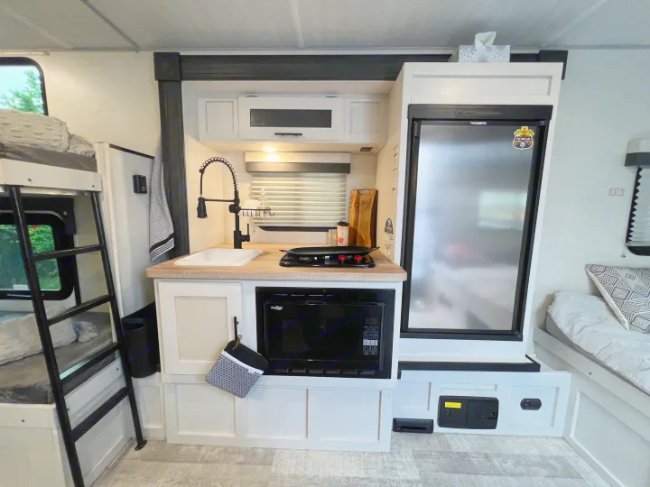 Inside this RV rental, a bright kitchen with sink, microwave, and fridge is central, with bunk beds left and a seating area right.. No Boundaries 16 2023