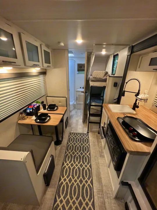 Cozy RV rental interior featuring a compact kitchen, dining area, and bunk beds, perfect for travel adventures.. No Boundaries 16 2023